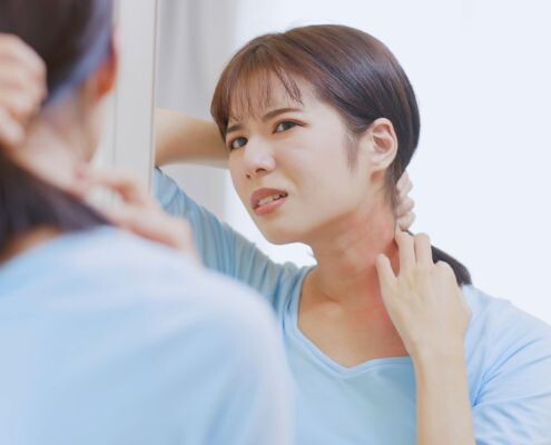 An Asian woman has skin allergies, so she scratches her neck in front of the mirror at home.