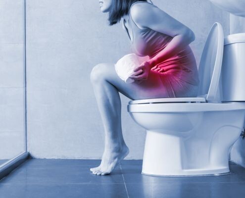 The woman sitting on the toilet feels uncomfortable with diarrhea in the bathroom