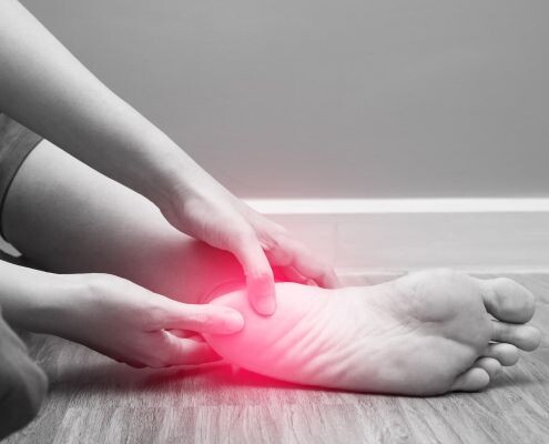 A woman sits on the ground with her hand pressing down on her heel, which is painful due to plantar fasciitis.