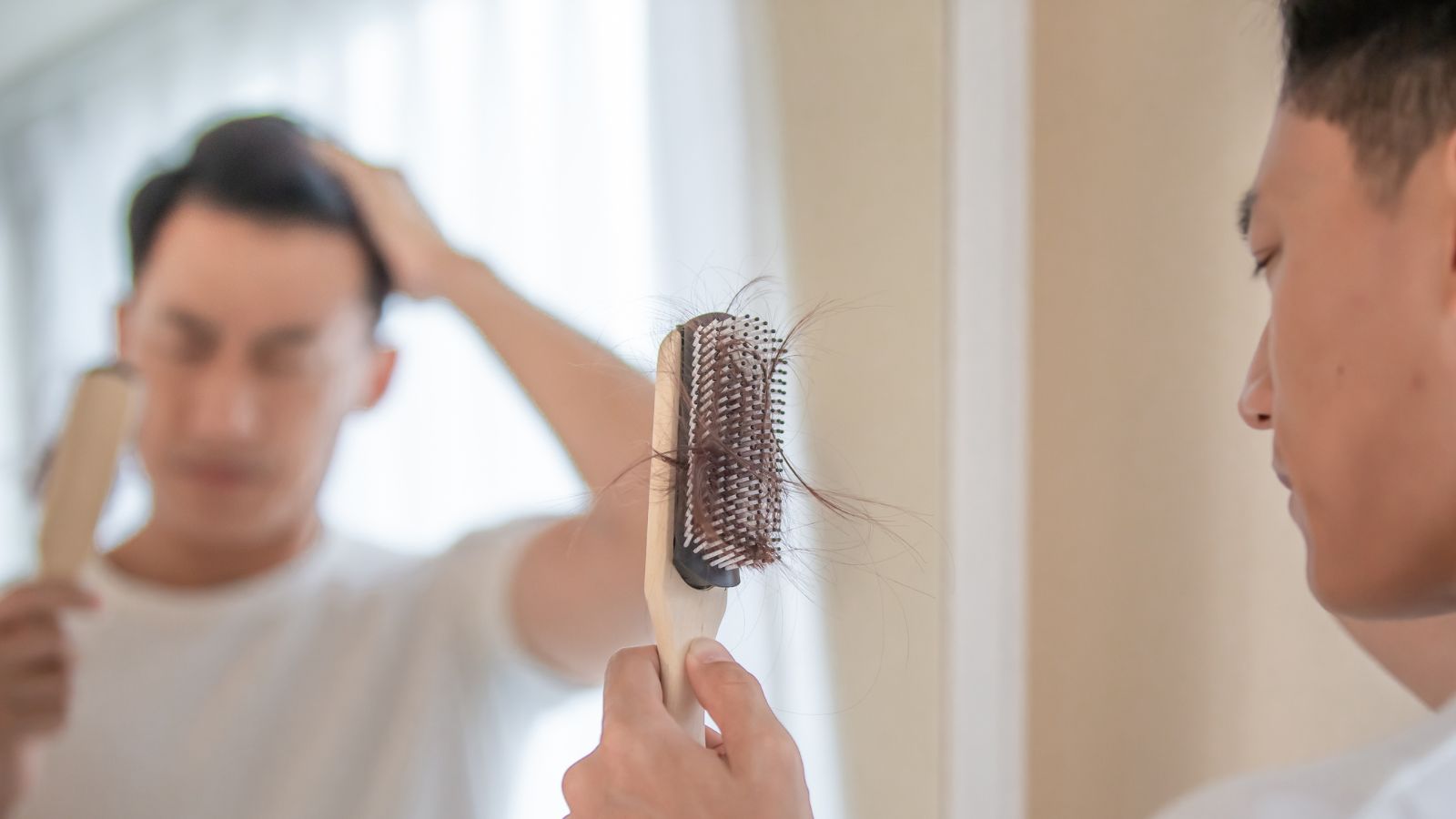 The Asian man notices that he has filled the comb with his fallen hair, which concerns him and raises suspicions about whether he is experiencing male pattern baldness symptoms
