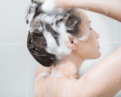 Woman in the shower washing hair with shampoo.