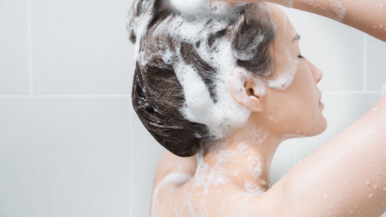 Woman in the shower washing hair with shampoo.